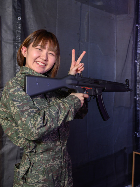 迷彩の女性がU2のマシンガンを打ち終わり、スッキリした笑顔でピースサイン