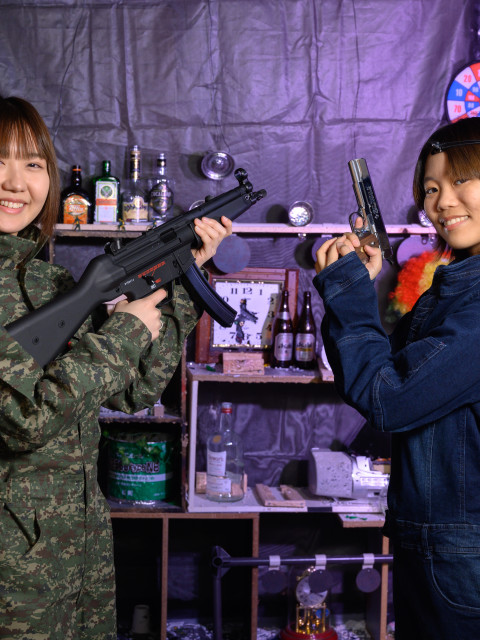 迷彩の女性がマシンガン、デニムの女性がハンドガンを持ち決めポーズ
